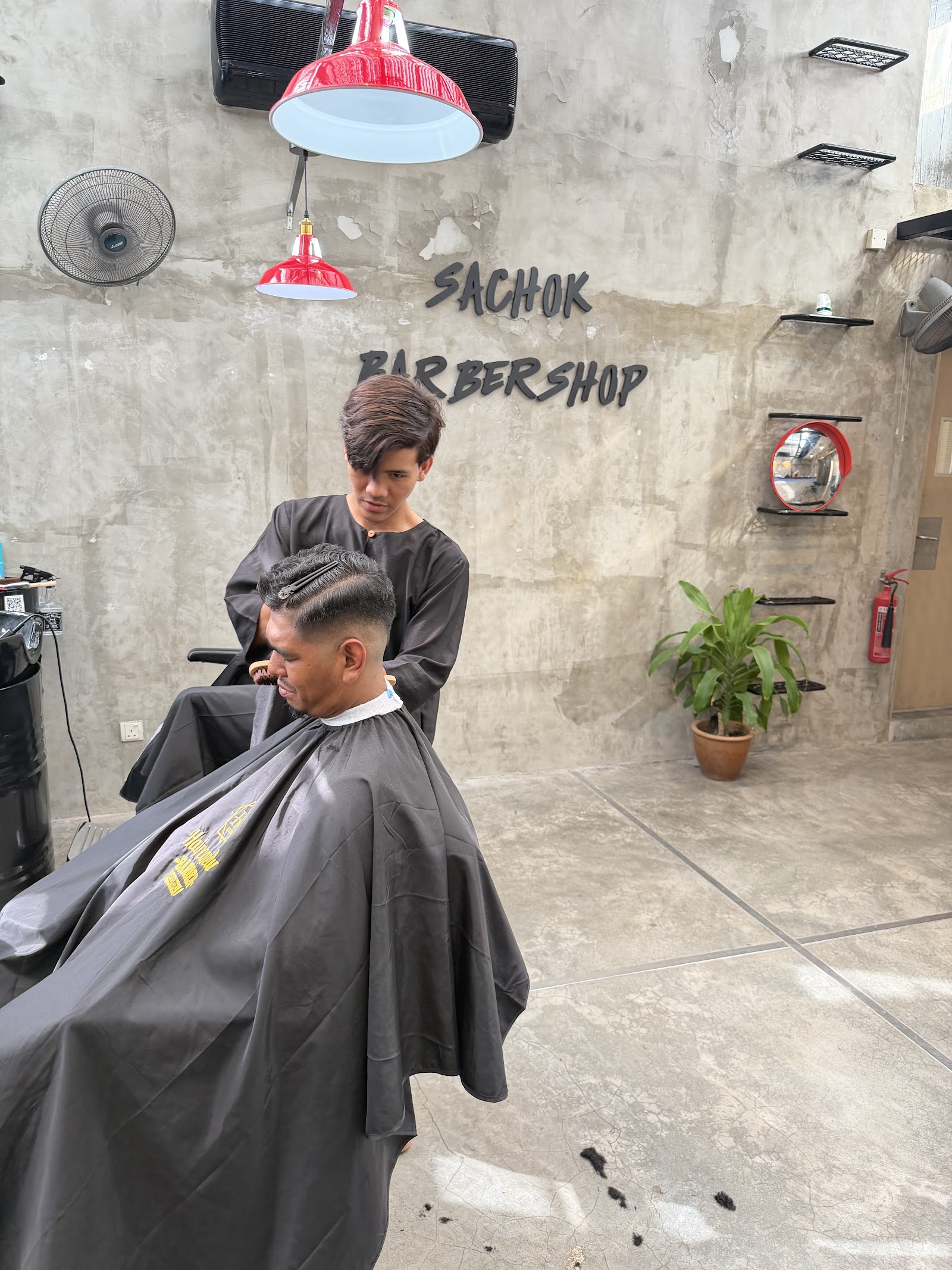 A barber at Sachok Barbershop finishing a client's fade against the shop's concrete wall