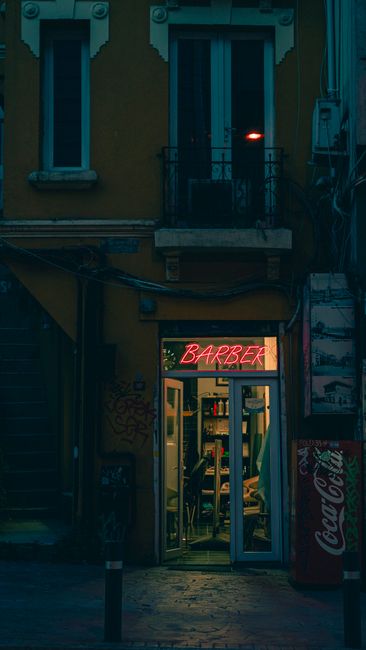 Neon barber sign glowing above a shop entrance at night